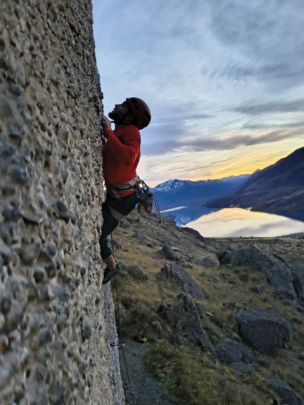 Persona escalando roca al atardecer frente a un lago patagónico