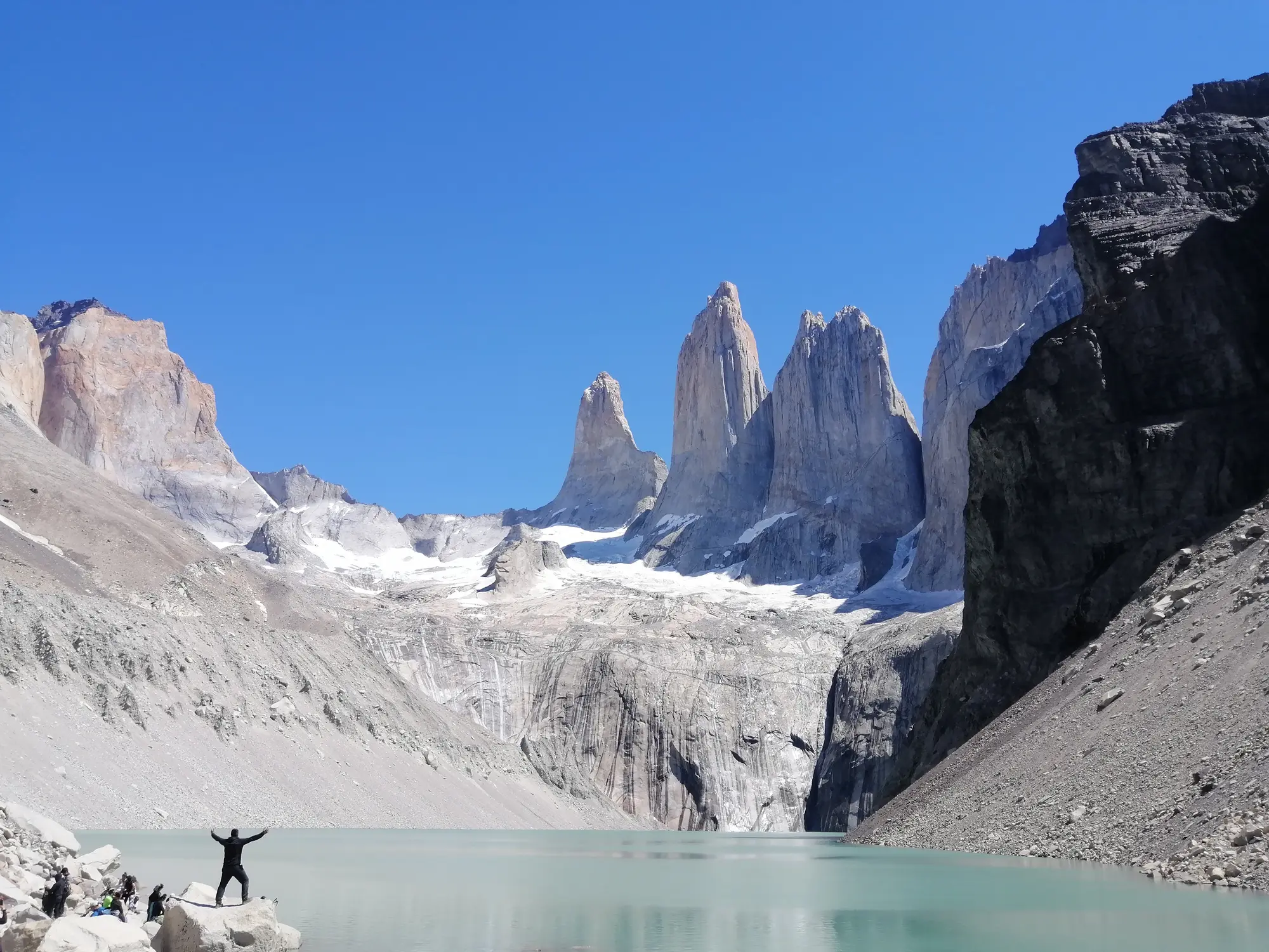 Excursionista con los brazos en alto frente a las Torres del Paine y una laguna turquesa, Patagonia chilena